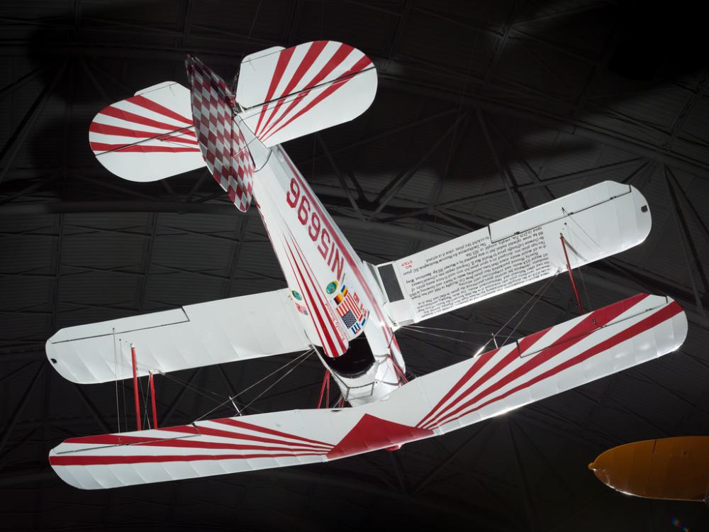 White and red painted single-engine aerobatic and military trainer biplane hanging in the museum.