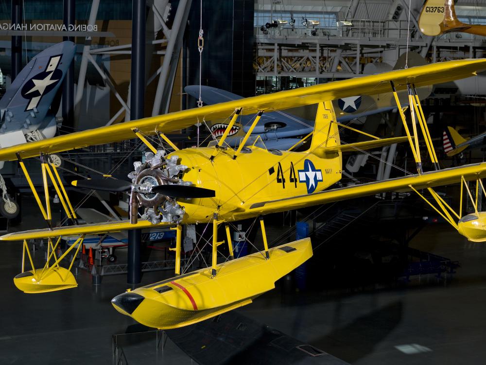 Bright yellow bi-plane with hand crank start hanging in the Steven F. Udvar-Hazy Center.