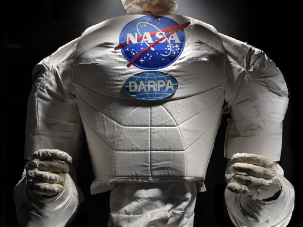 Frontal view of a body of a robot with arms, chest with a NASA logo, and an orange face cover.