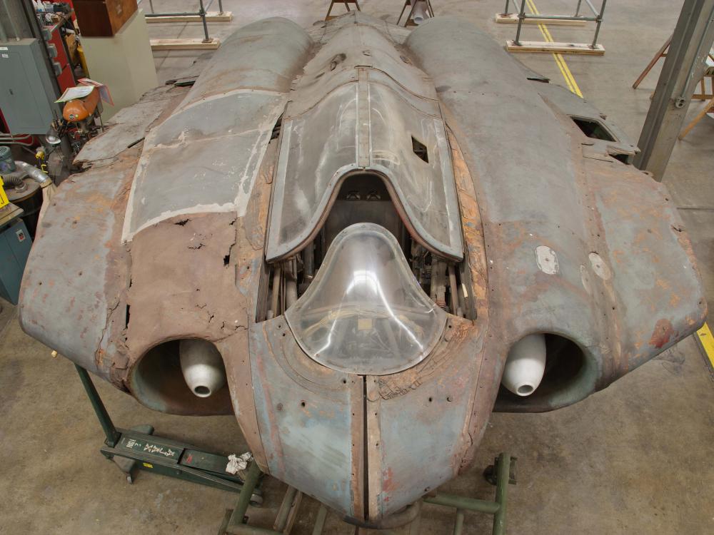 Top view of a gray, World War II era aircraft. On the left side, fairings (material covering gaps on an aircraft) on the aircraft are more rusted in comparison to the right side.