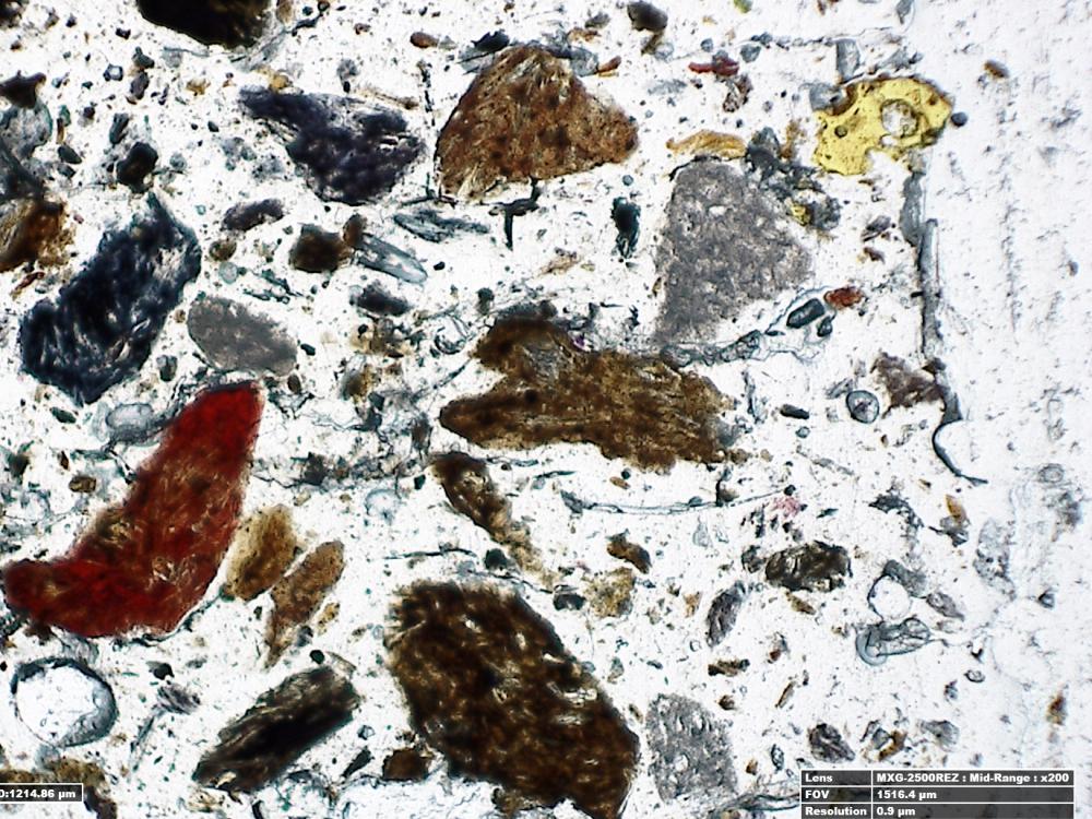 A microscopic view of a thin section of adhesive sampled from a World War II era aircraft, with various particles of various colours intertwined with the adhesive.