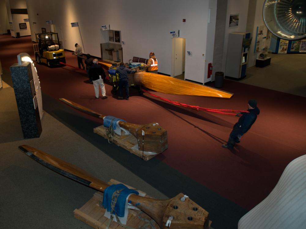 Museum staff members move parts of a large wind tunnel fan around other objects inside the Museum.