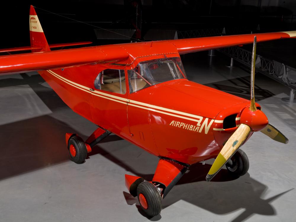 Diagonal front view of red monoplane with yellow accent colors and one engine. Fixed landing gear is used to make the aircraft roadable.