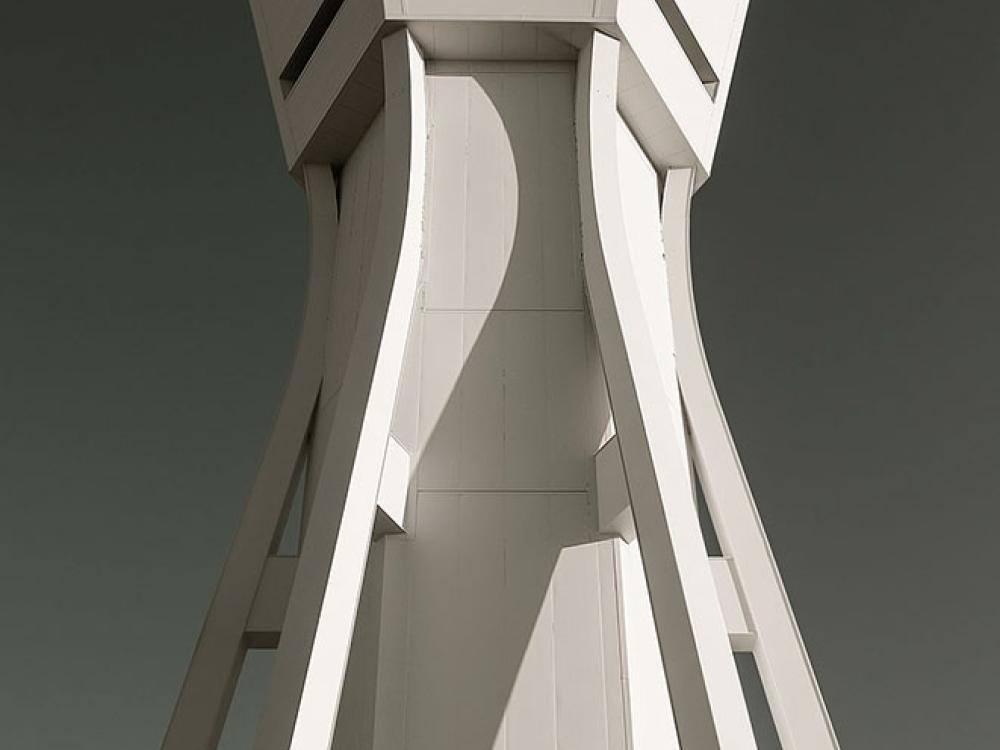 An air traffic control tower with light-colored, contemporary style supports. Near the top, a base for operations has at least three sides for different perspectives of observation.