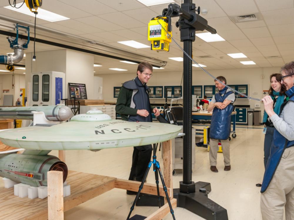 Four members of Smithsonian staff work together to prepare the Starship Enterprise, a dish-shaped, gray spaceship, for an X-ray scan.