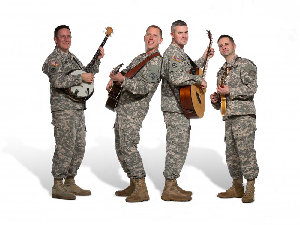 A group of four men in Army uniform pose informally with their instruments. The person on the far left is playing a banjo while everyone else seems to be playing guitar.