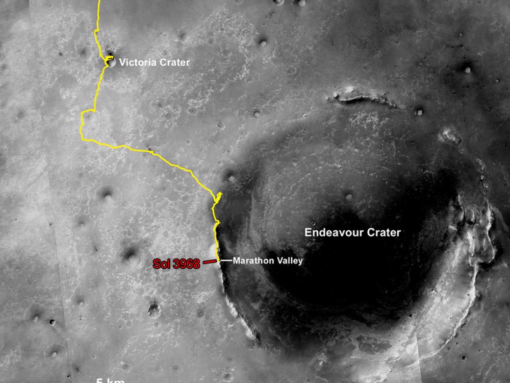 A partial, black and white satellite view of Mars with a yellow line describing the movement made by Opportunity, a Mars rover, between multiple craters.