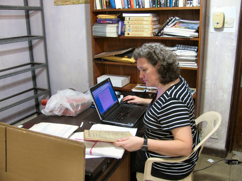 A white, female Museum archivist examines documents owned by author Arthur C. Clarke inside his home.