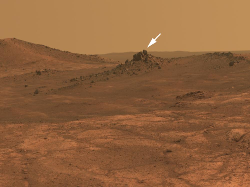 A hilly landscape on Mars with a small white arrow pointing to a crater named after a historic aircraft, the "Spirit of St. Louis".