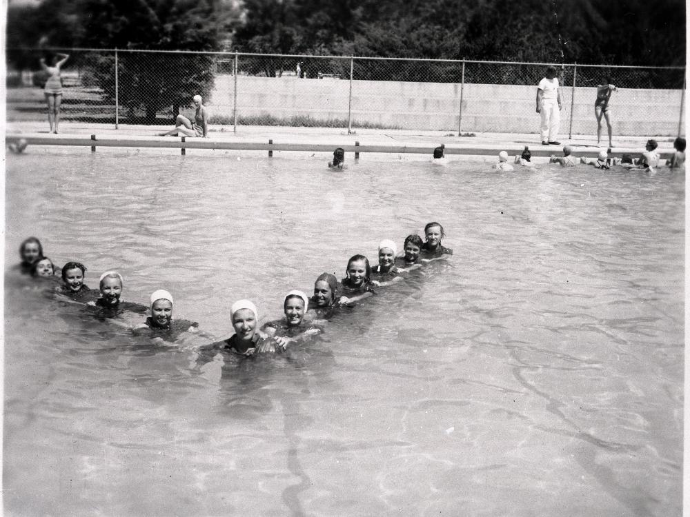 A group of female pilots in training during World War II swim together in a triangle formation in a pool.