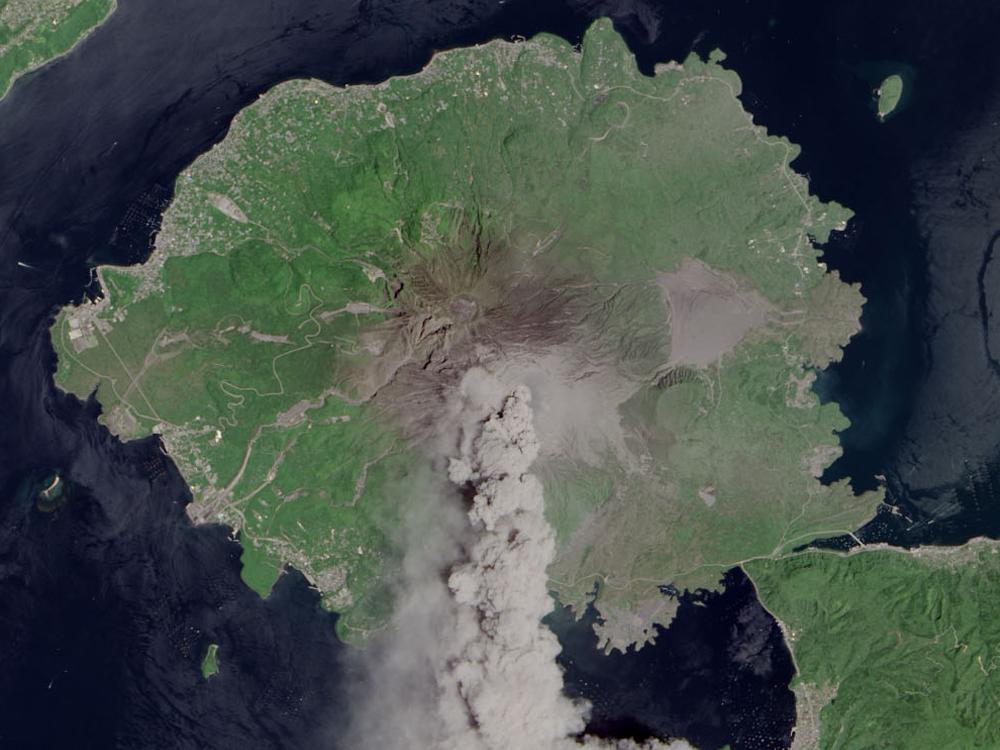 Satellite view of Sakura-jima, a volcano in Japan, during an eruption. Plumes of smoke are in the atmosphere above the volcano.