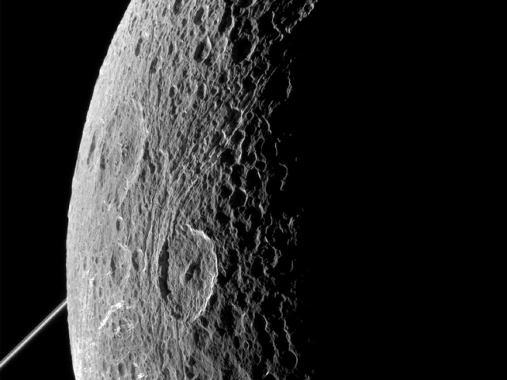 Partial view of a moon belonging to Saturn. The edge is lit by the Sun whereas the rest is facing away from the Sun.