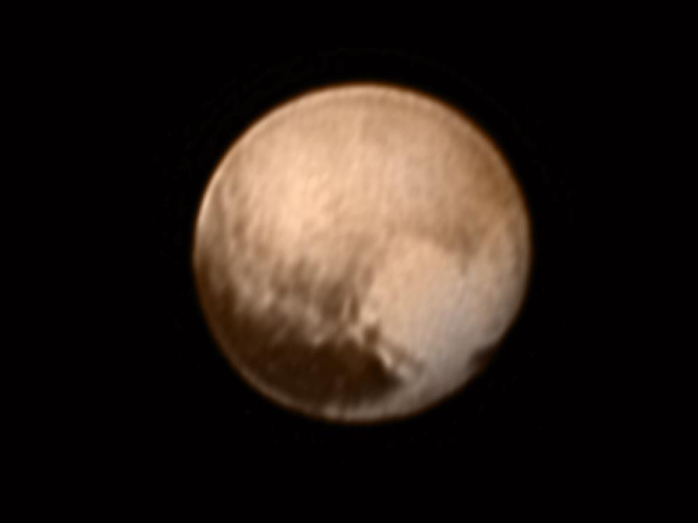 Disk view of Pluto, showing a brown planet with a heart-like shape coloration on the lower right quadrant of the dwarf planet.