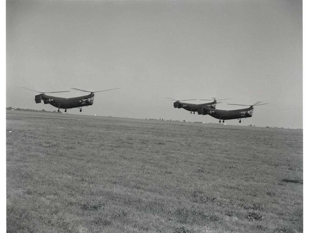 Three helicopters with two sets of propellors apiece vertically fly together during an airshow.