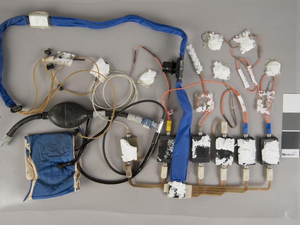 A during-conservation view of an blue Apollo program medical instrumentation harness. Majority of the harness and various parts have been removed from its previous white board.