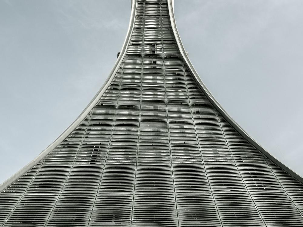 Air traffic control tower with a vial-shaped support structure that expands at the bottom from a narrow top. The support structure looks to be made from sections of steel.