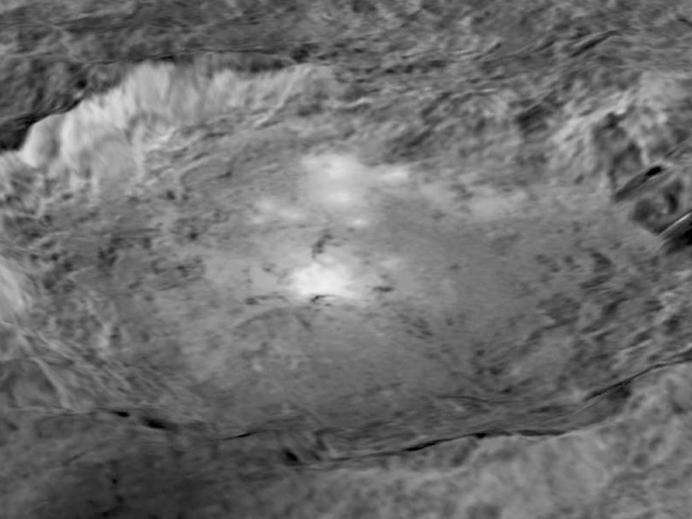 Black and white, close-up view of a large crater on Ceres, a dwarf planet. The crater has a shape similar to an oval.