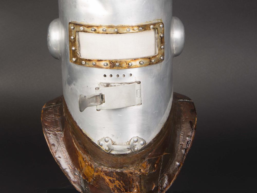 Frontal view of the first pressure helmet. The helmet is made from metal and is experiencing white-colored corrosion, requiring conservation treatment.