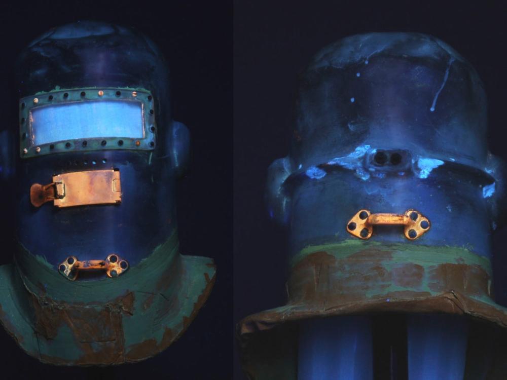 Side-by-side views of the Wiley Post pressure helmet, with the front visible on the left and the back visible on the right. Views are taken from ultraviolet light intended to discover corrosion products used on the helmet.