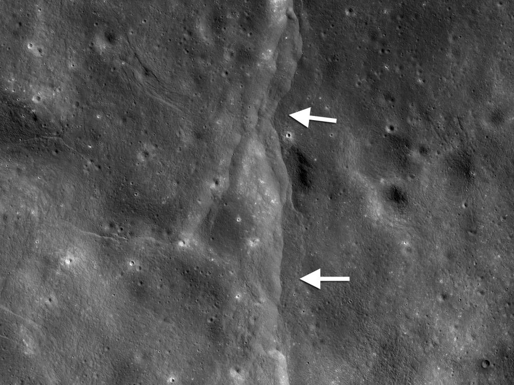 View of fault scarps, where land on one side has moved vertically, on the Moon. White arrows point out the fault line.