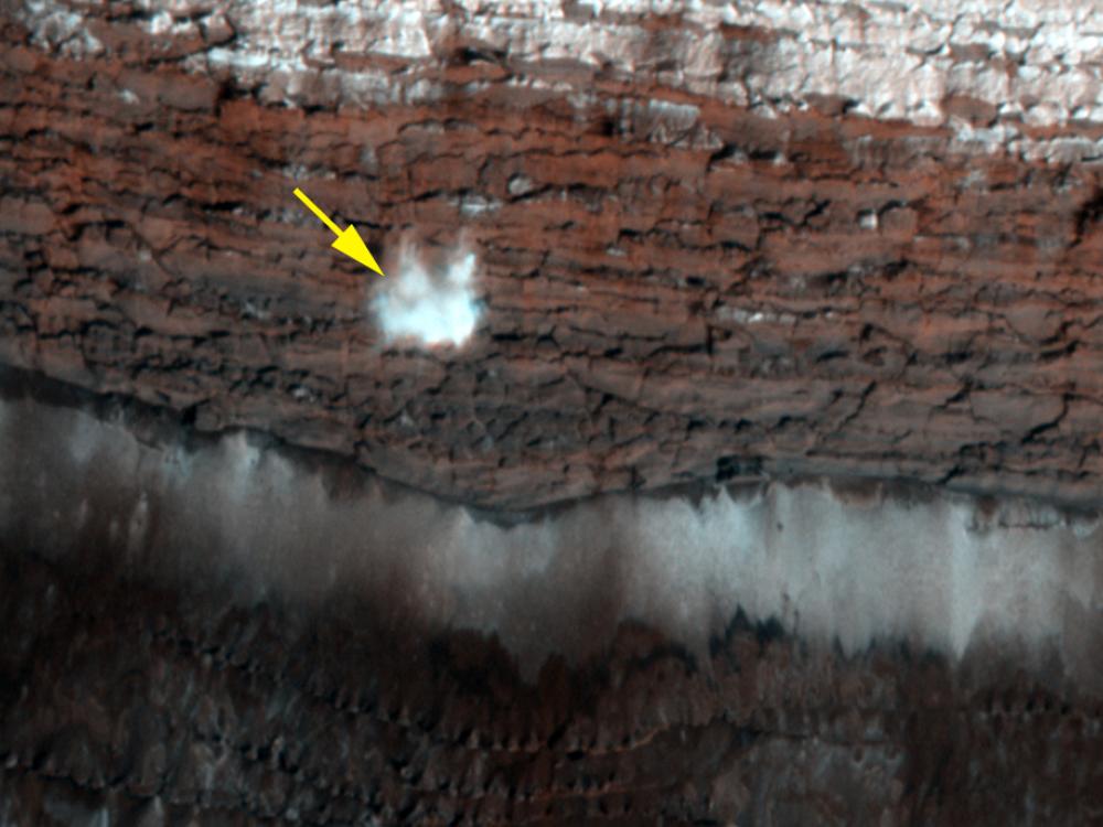 A frost-covered cliff on the northern polar surface of Mars. A yellow arrow points out potential frost that is in the process of freefalling.