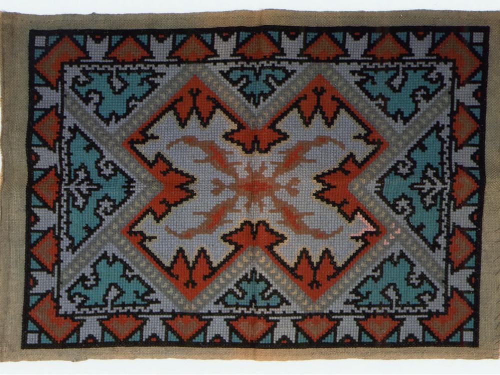 Orange, blue, and white knitted rug with intricate X-letter shape pattern.