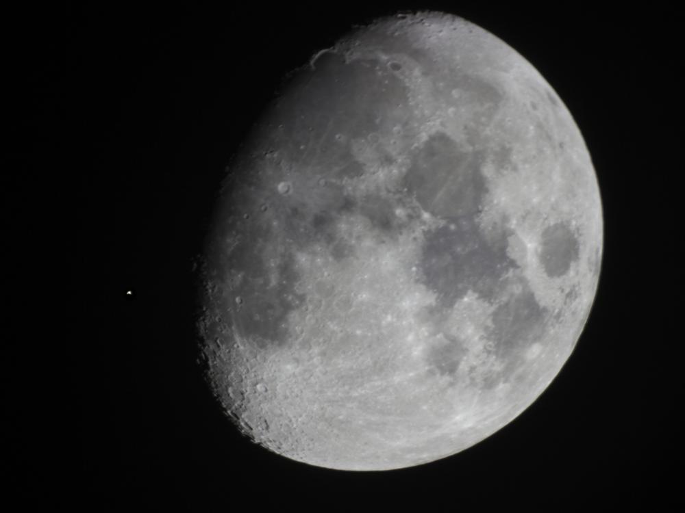 The moon, seen as larger than a quarter moon, is nearly covering a bright star in the sky on its left.