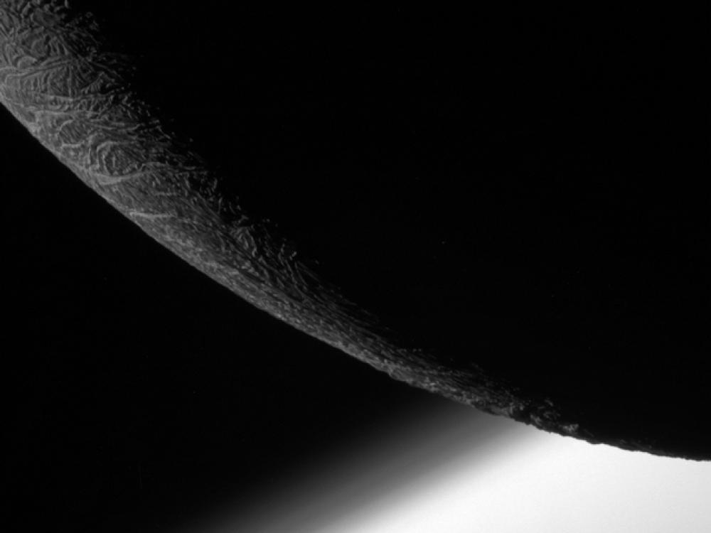 Partial view of the mostly non-illuminated Enceladus, a moon of Saturn.