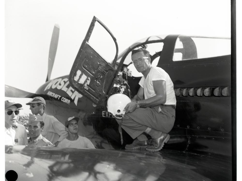 Robert Eucker, a white male aviator, stands on the wing of his aircraft. He is holding a white helmet.