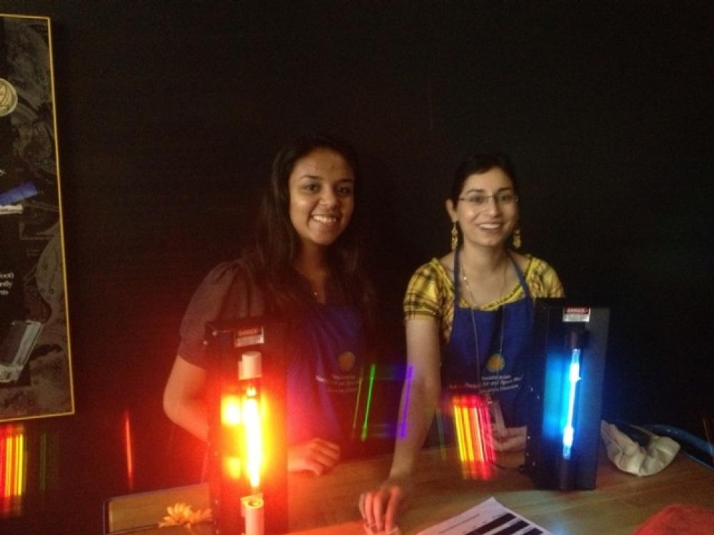 Two student volunteers host an station designed to educate children at the museum. At this station, they are holding colored gas devices.