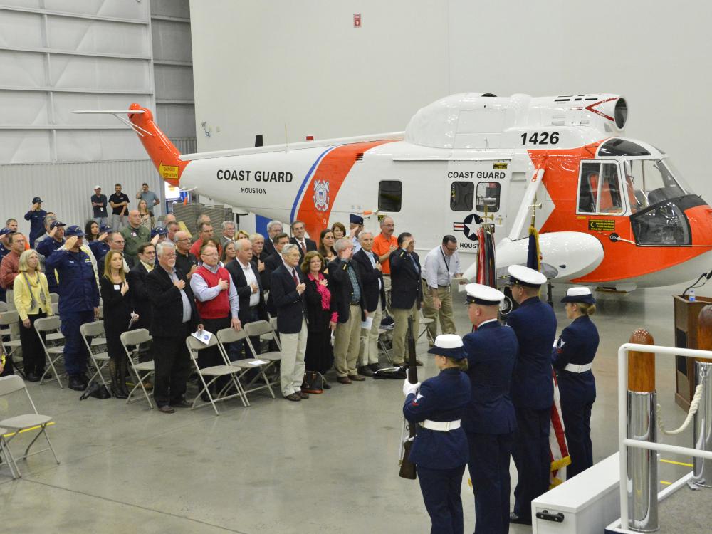 A group of people stand together for a ceremony following the restoration of an orange and white helicopter on their left .