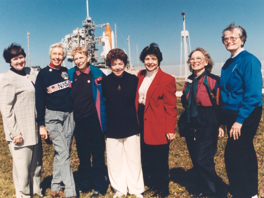 Seven women who trained to become astronauts in 1961 pose together in front of a Space Shuttle launch in 1995.