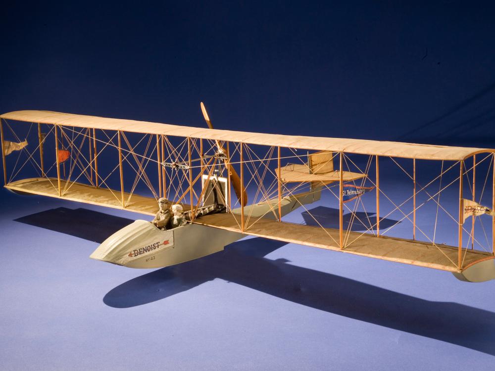 Wooden biplane-airboat model with space for two people, a passenger and the pilot. Flaglets are placed on the front structure in between the wings.