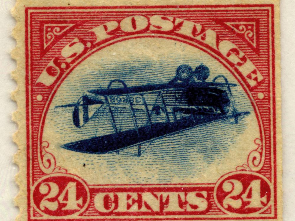 View of red, U.S. Air Mail postage stamp that has an error of the Jenny biplane facing upside down.