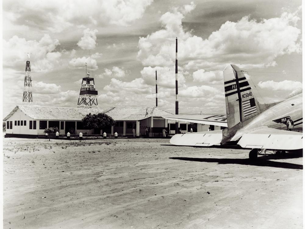 Part of the tarmac at Barreiras Airport in Brazil. Nearby are a one story building and the rear of a commercial aircraft.