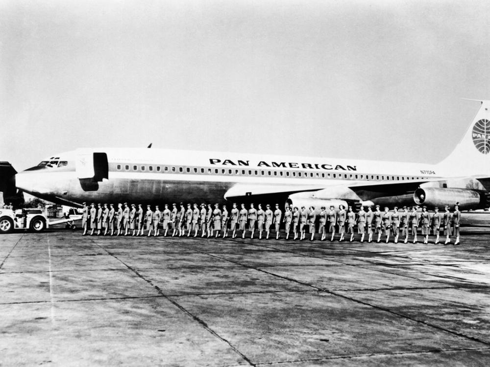 A group of Pan American Airways flight attendants board a commercial jet in a straight line.