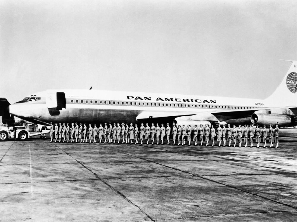 A group of Pan American Airways flight attendants board a commercial jet in a straight line.