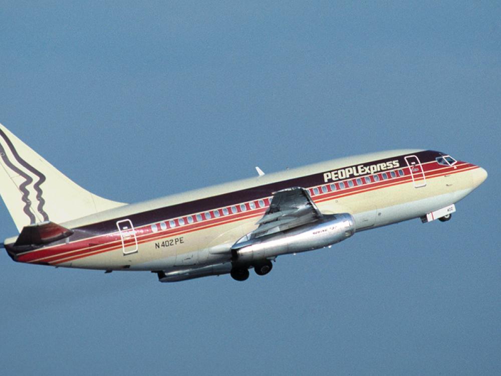 Side view of commercial aircraft in flight. Aircraft has at least two engines and red, black, and white PeoplExpress