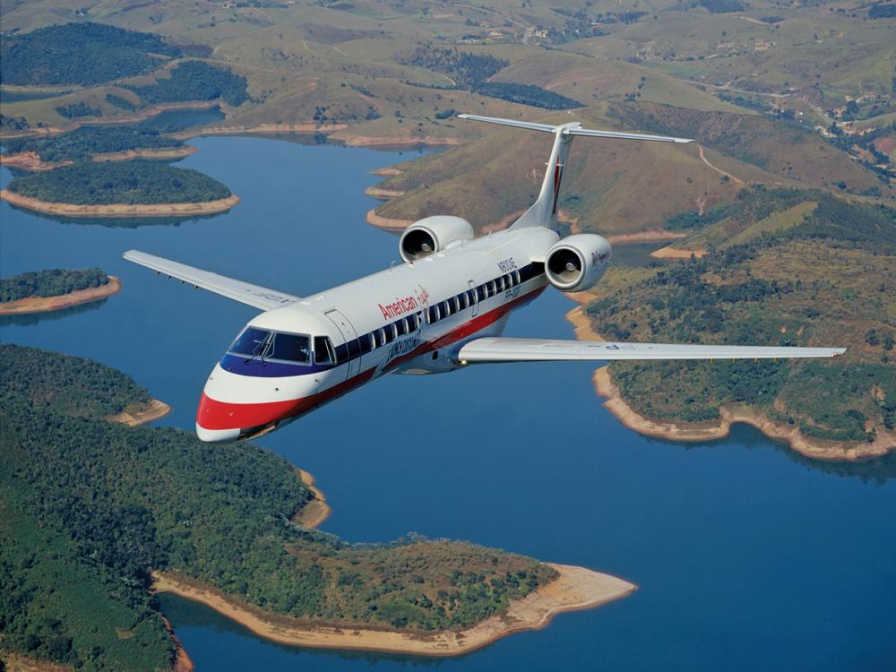 Front view of commercial jet in flight. The jet has two engines placed near the rear of the plane and white, blue, and red American Eagle livery.