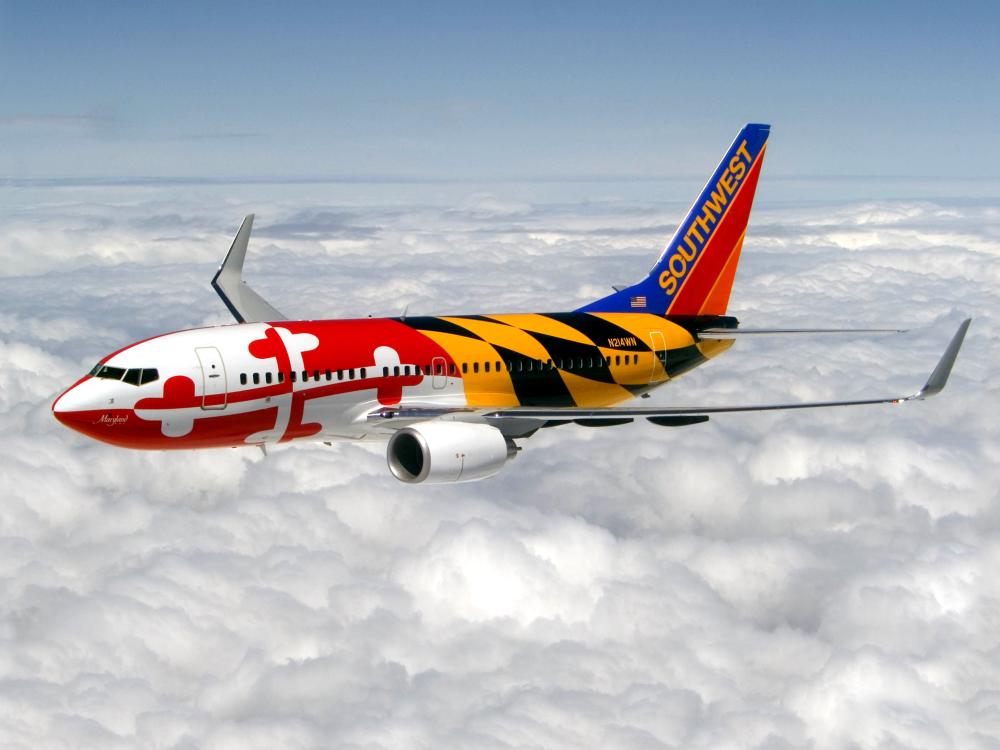 Side view of commercial aircraft in flight. Airccraft features two engines and red, white, yellow, and black Southwest Airlines livery that features the pattern of the Maryland state flag.