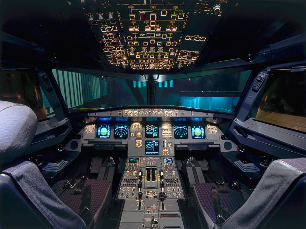 View of the front of a commercial aircraft's cockpit, with two pilot seats and the top and center panels in view.