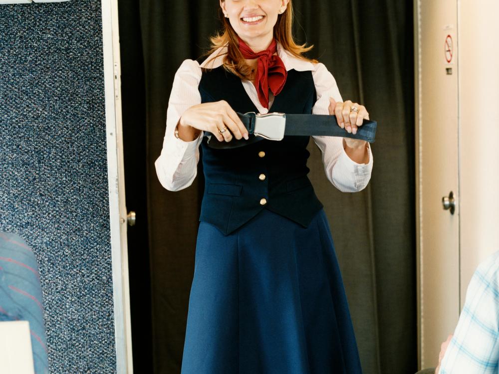 A female flight attendant holds a seat belt as part of a passenger safety demonstration.