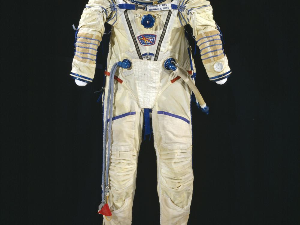 White pressure suit with blue trim and multiple plugs and tubes