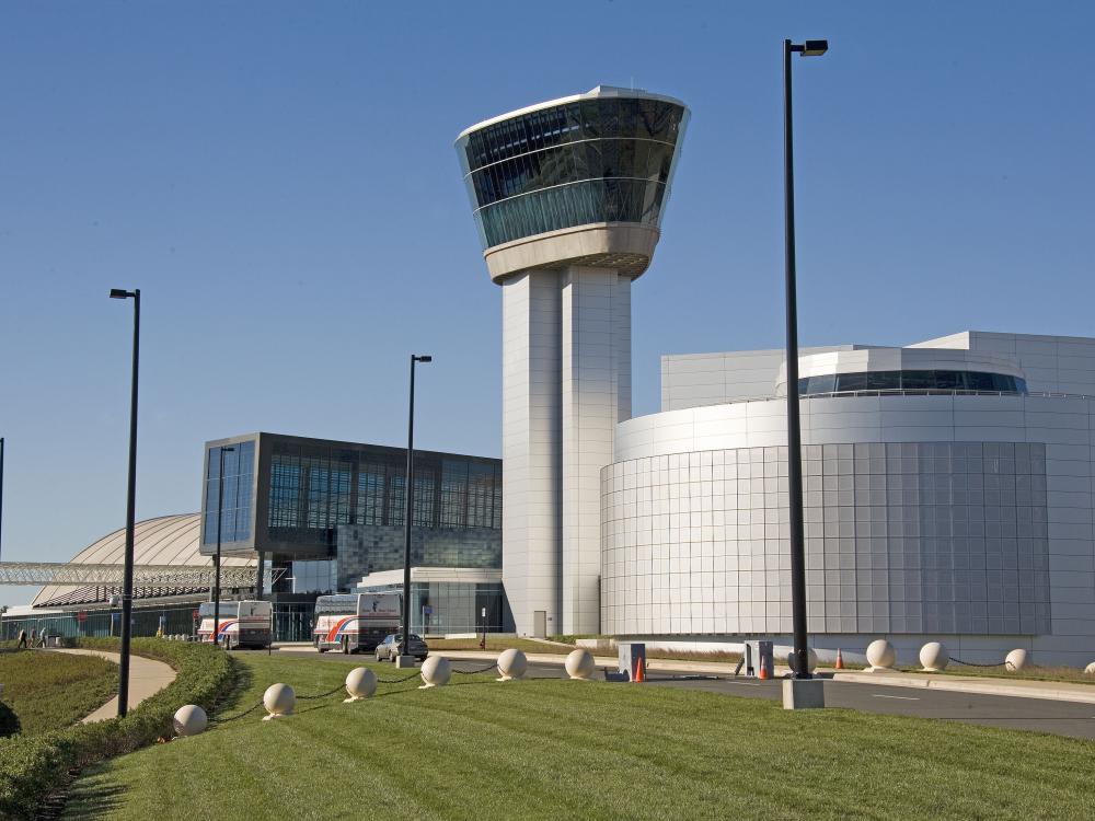 One side of large silver building with circular theater in foreground and Tower with glass-enclosed observation deck at top.