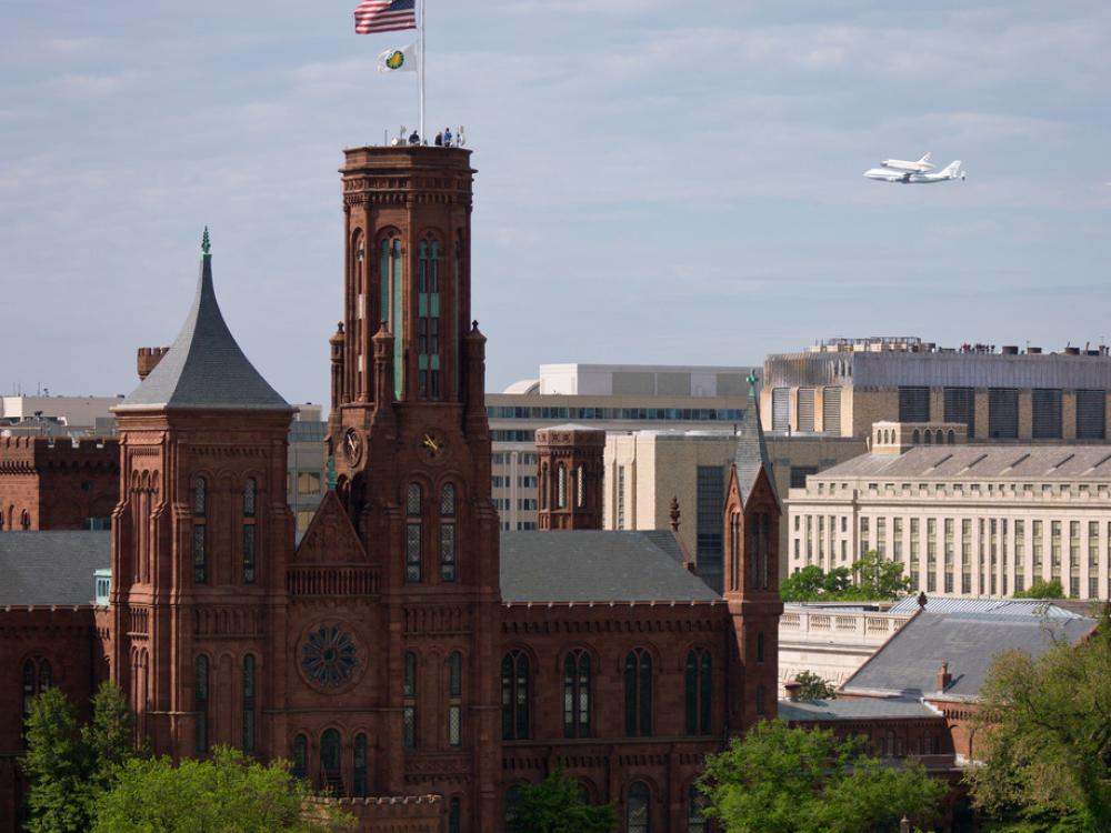 Space Shuttle Discovery, attached to an aircraft modified for shuttle transportation, flies near the Smithsonian Castle in Washington, D.C.