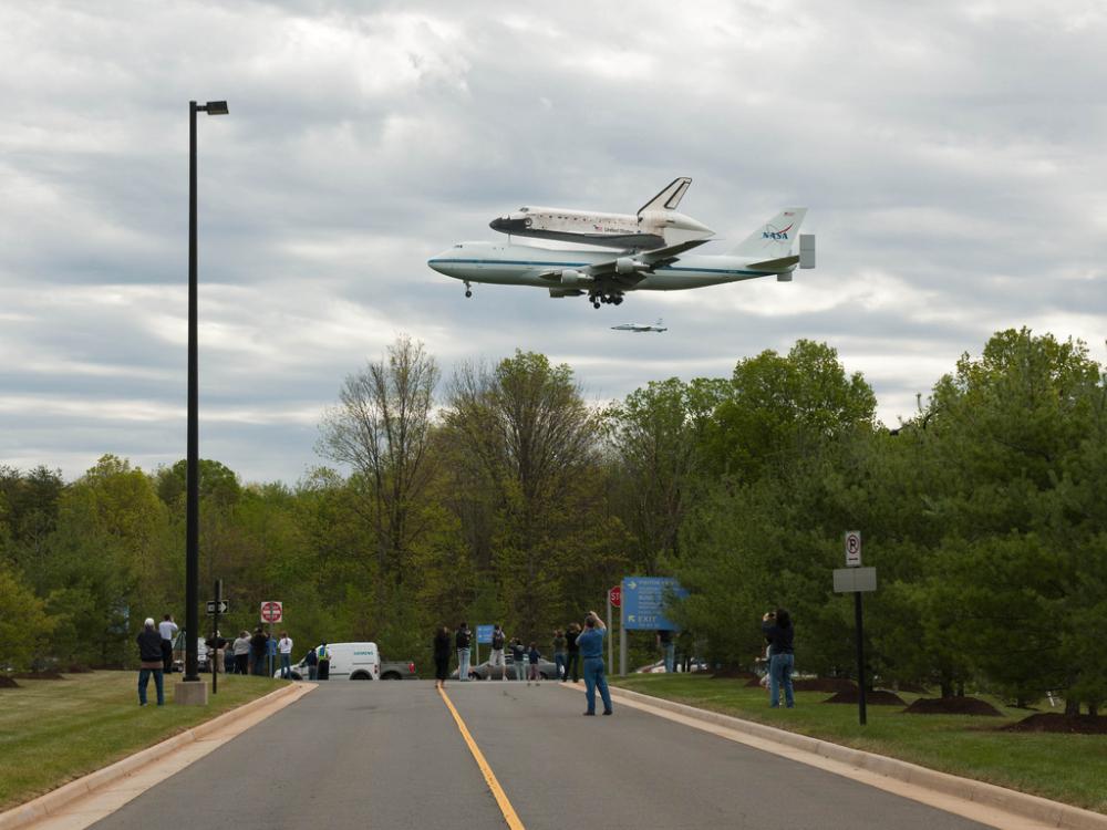 Space Shuttle Discovery prior to landing at Washington Dulles International Airport. It is flying low, so spectators get a good look at the shuttle and the shuttle transport aircraft.