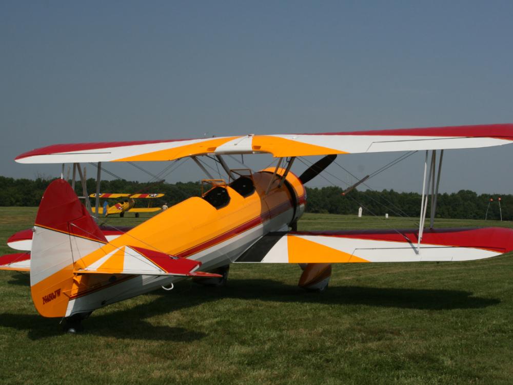 Back view of yellow, red, and white biplane with single engine.