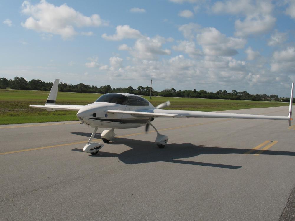 Frontal view of white monoplane with long wings and fixed landing gear.