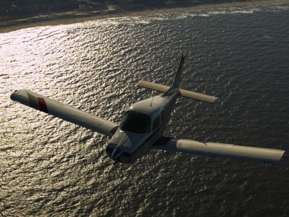 Front view of a monoplane with one engine flying above a body of water.