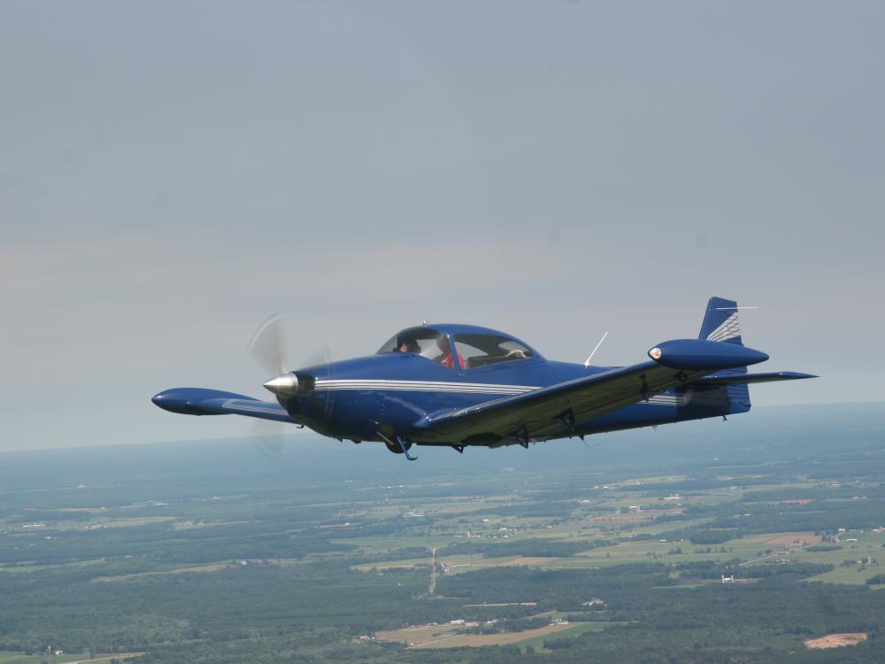 Side view of blue monoplane with a single engine in flight.